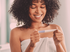 Smiling woman wrapped in a towel looking at a pregnancy test.