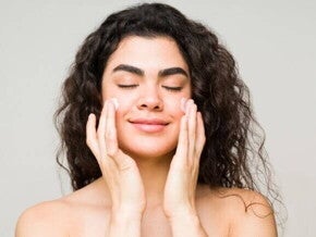 Mulher espalhando creme hidratante no rosto, de olhos fechados