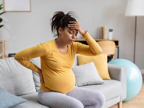 mulher grávida com uma das mãos nas costas e outra posicionada na testa, com olhos fechados e assoprando com a boca mulher grávida com uma das mãos nas costas e outra posicionada na testa, com olhos fechados e assoprando com a boca