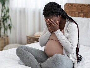 Mulher grávida sentada na cama cobrindo o rosto com as mãos.
