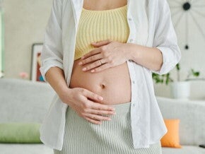 Mulher grávida com as mãos apoiadas na barriga, destacando o início da gestação.
