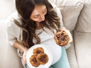 mulher grávida segurando um prato com cookies de chocolate e sorrindo.
