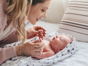 mãe sorrindo e brincando com o bebê recém-nascido na cama. mãe sorrindo e brincando com o bebê recém-nascido na cama.