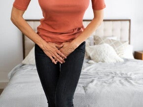 mulher com as pernas cruzadas com as mãos em cima da vagina