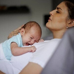 Uma mãe com aspecto de cansaço, deitada com um bebê chorando em seu colo. Uma mãe com aspecto de cansaço, deitada com um bebê chorando em seu colo.