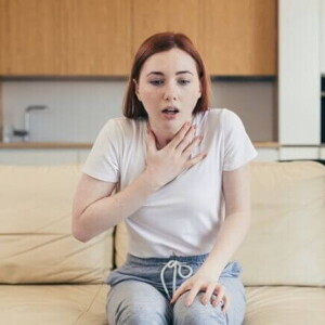 Mulher sentada em um sofá com uma das mãos sobre o pescoço e a boca levemente aberta Mulher sentada em um sofá com uma das mãos sobre o pescoço e a boca levemente aberta