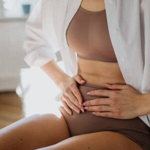 Mulher sentada com as mãos sobre o abdômen, sentindo dor pélvica