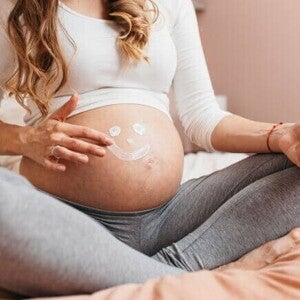 gestante aplicando creme na barriga com desenho de carinha sorridente.