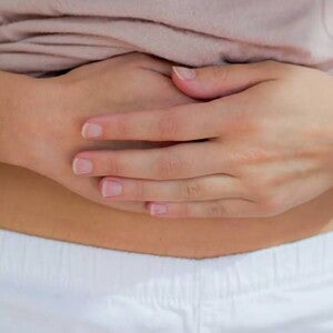 Mulher com cólica menstrual pressionando com força a região abaixo do umbigo.