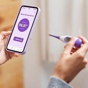 mulher segurando celular e termômetro ao monitorar temperatura basal. mulher segurando celular e termômetro ao monitorar temperatura basal.