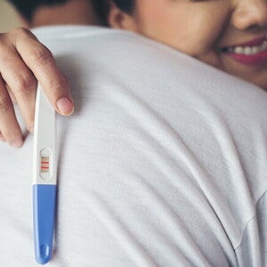 Uma mulher abraçando o marido enquanto segura um teste de gravidez