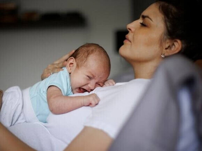 Uma mãe com aspecto de cansaço, deitada com um bebê chorando em seu colo. Uma mãe com aspecto de cansaço, deitada com um bebê chorando em seu colo.