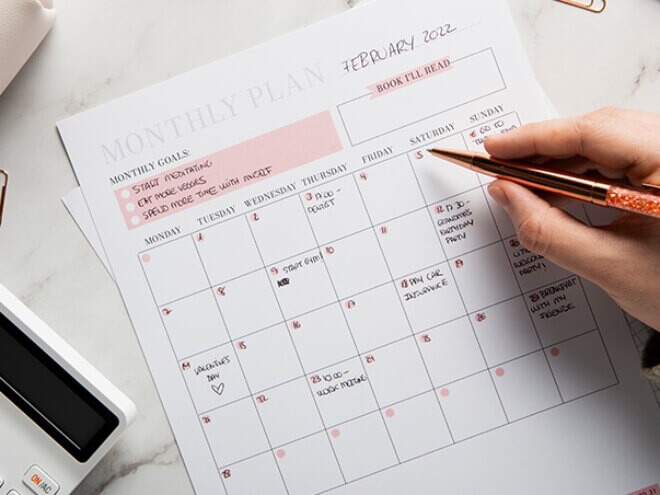 Na imagem, uma mão segura uma caneta diante de um calendário do mês Na imagem, uma mão segura uma caneta diante de um calendário do mês
