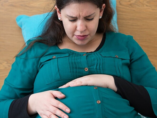 Mulher grávida sentada na cama com semblante de preocupação embalando sua barriga Mulher grávida sentada na cama com semblante de preocupação embalando sua barriga