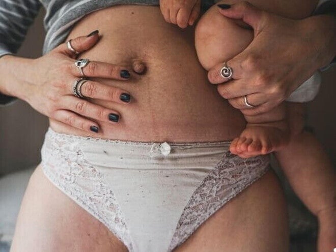 Close na barriga de uma mulher no pós parto usando uma calcinha de cor clara, segurando seu bebê no colo e apoiando outra mão na barriga. Close na barriga de uma mulher no pós parto usando uma calcinha de cor clara, segurando seu bebê no colo e apoiando outra mão na barriga.