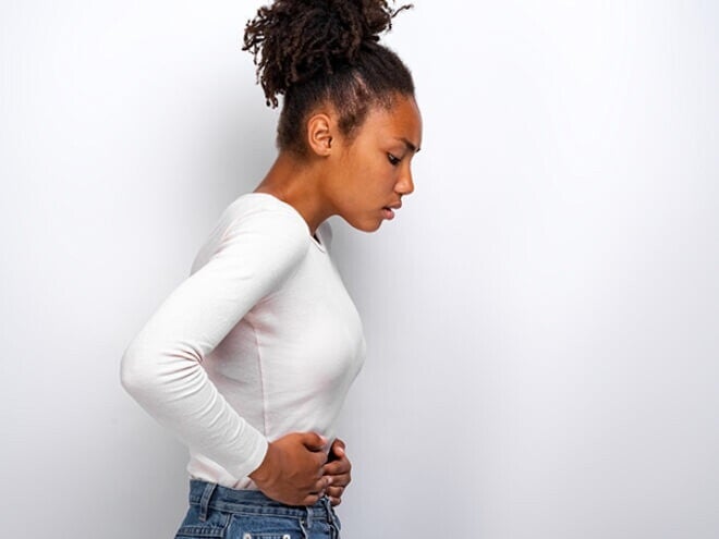 Mulher vestindo blusa branca com as mãos na barriga e expressão de desconforto Mulher vestindo blusa branca com as mãos na barriga e expressão de desconforto