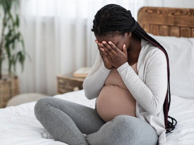Mulher grávida sentada na cama cobrindo o rosto com as mãos. Mulher grávida sentada na cama cobrindo o rosto com as mãos.