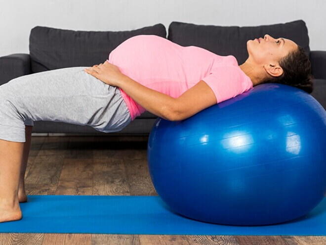 Gestante com as costas apoiadas em uma bola inflável praticando fisioterapia pélvica. Gestante com as costas apoiadas em uma bola inflável praticando fisioterapia pélvica.
