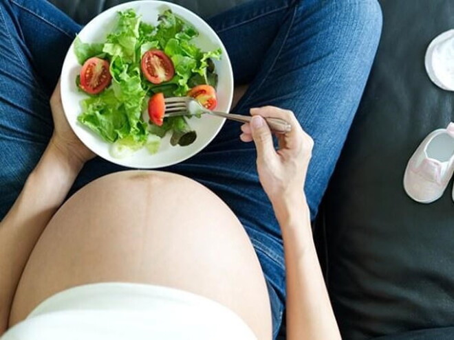 Gestante sentada em um sofá saboreando uma salada saudável Gestante sentada em um sofá saboreando uma salada saudável