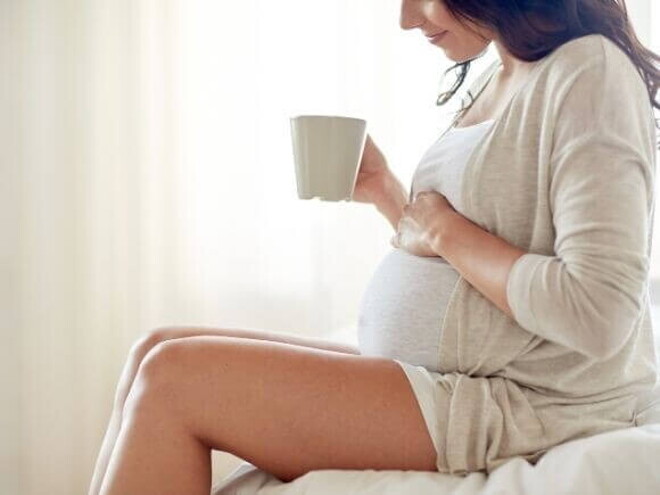 Mulher grávida sentada com uma caneca na mão Mulher grávida sentada com uma caneca na mão