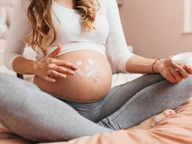 gestante aplicando creme na barriga com desenho de carinha sorridente. gestante aplicando creme na barriga com desenho de carinha sorridente.