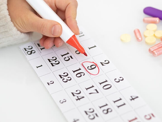 Imagem de uma pessoa fazendo anotações em um calendário em meio a comprimidos e objetos diversos Imagem de uma pessoa fazendo anotações em um calendário em meio a comprimidos e objetos diversos