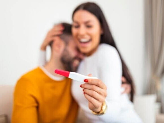 Mulher feliz segurando um teste de gravidez na mão e sendo abraçada por um homem, sugerindo comemoração pelo resultado positivo Mulher feliz segurando um teste de gravidez na mão e sendo abraçada por um homem, sugerindo comemoração pelo resultado positivo