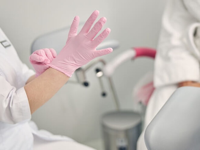 Paciente sentada em cadeira ginecologia enquanto médica se prepara para examiná-la Paciente sentada em cadeira ginecologia enquanto médica se prepara para examiná-la