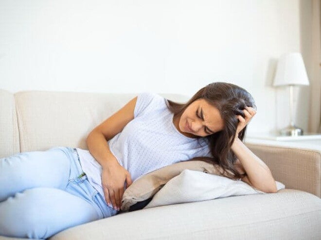 mulher com blusa branca deita no sofá sentindo cólicas abdominais