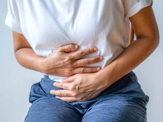 mulher com usando camiseta branca, levemente curvada e com as mãos posicionadas na barriga mulher com usando camiseta branca, levemente curvada e com as mãos posicionadas na barriga