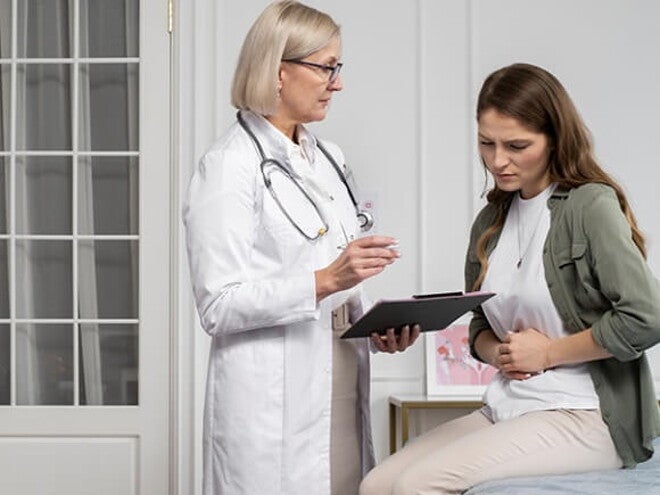 Mulher sentada em uma cama de hospital discutindo sua condição médica com uma profissional de saúde Mulher sentada em uma cama de hospital discutindo sua condição médica com uma profissional de saúde