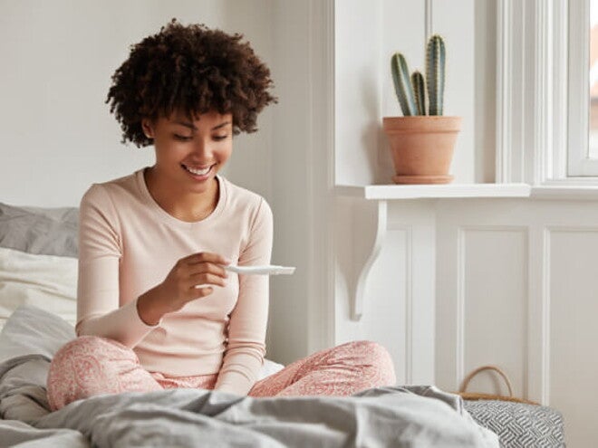 Mulher sentada na cama olhando feliz para um teste de gravidez Mulher sentada na cama olhando feliz para um teste de gravidez