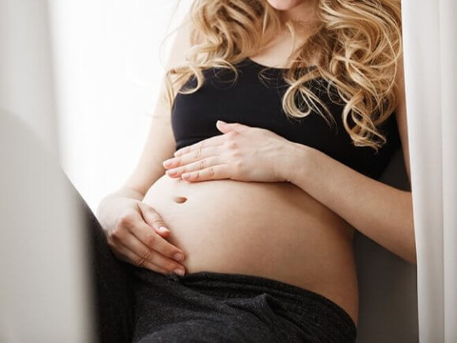 Gestante sentada com as mãos sobre a sua barriga