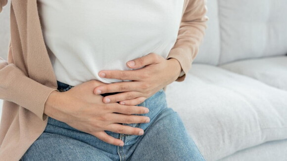 Mulher sentada em um sofá, com as mãos sobre a região uterina Mulher sentada em um sofá, com as mãos sobre a região uterina