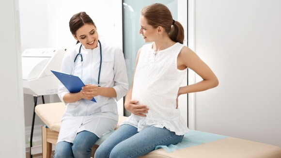 Médica avaliando paciente grávida, as duas estão sentadas na maca Médica avaliando paciente grávida, as duas estão sentadas na maca