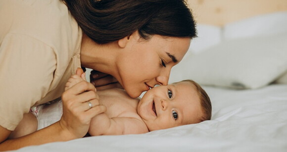 Bebê deitado na cama recebendo carinho da sua mãe Bebê deitado na cama recebendo carinho da sua mãe