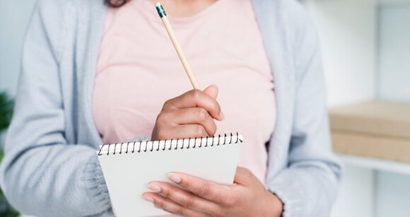Mulher vestindo blusa rosa e casaco azul com caderno e lápis em mãos Mulher vestindo blusa rosa e casaco azul com caderno e lápis em mãos