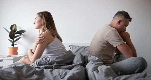 Casal sentados na cama de costas um para o outro.
