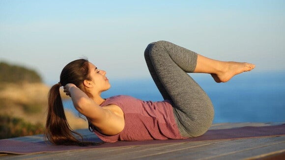 Uma mulher deitada em um espaço ao ar livre, fazendo um exercício abdominal