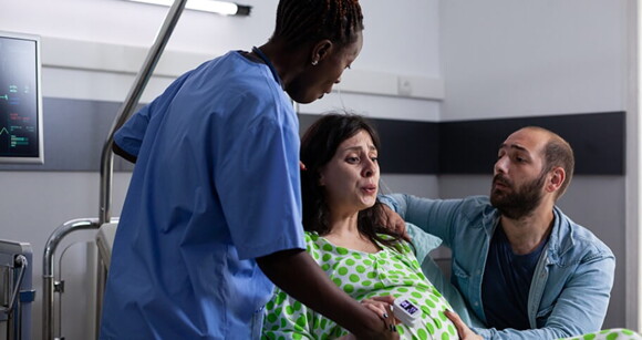 Gestante em um ambiente hospitalar em trabalho de parto sendo amparada pelo marido e por uma doula Gestante em um ambiente hospitalar em trabalho de parto sendo amparada pelo marido e por uma doula