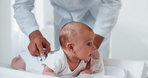 Médico avaliando bebê deitado de bruços em consultório Médico avaliando bebê deitado de bruços em consultório