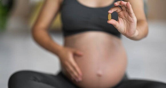 gestante sentada com uma mãe na barriga e a outra segurando uma cápsula gestante sentada com uma mãe na barriga e a outra segurando uma cápsula