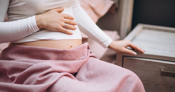 Mulher grávida sentada em uma cama tocando suavemente sua barriga Mulher grávida sentada em uma cama tocando suavemente sua barriga