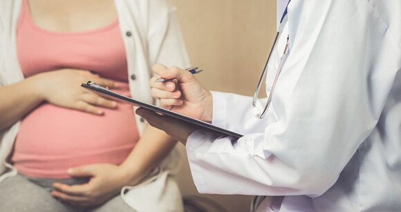 Médico fazendo anotações em uma prancheta ao lado de uma mulher grávida sentada na cadeira Médico fazendo anotações em uma prancheta ao lado de uma mulher grávida sentada na cadeira