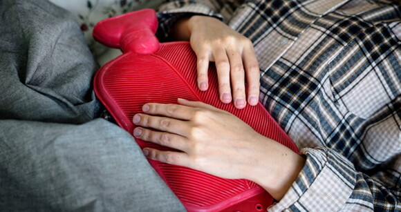 Mulher deitada na cama com uma bolsa de compressa quente sobre a barriga para aliviar desconforto pélvico Mulher deitada na cama com uma bolsa de compressa quente sobre a barriga para aliviar desconforto pélvico