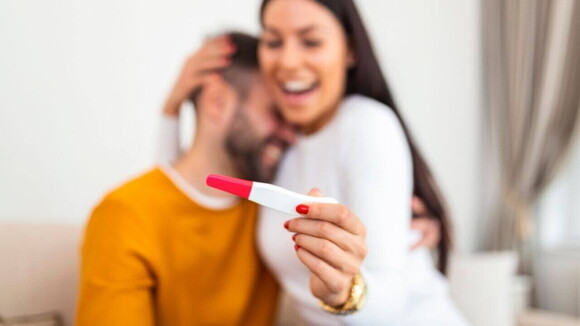 Mulher sorrindo e abraçando um homem, enquanto segura um teste de gravidez na mão Mulher sorrindo e abraçando um homem, enquanto segura um teste de gravidez na mão