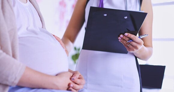 Médica avaliando uma gestante com a mão sobre a sua barriga Médica avaliando uma gestante com a mão sobre a sua barriga