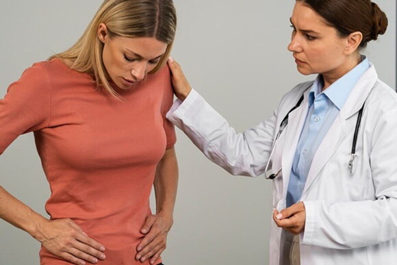 Médica olhando para a paciente enquanto ela apalpa o abdômen Médica olhando para a paciente enquanto ela apalpa o abdômen