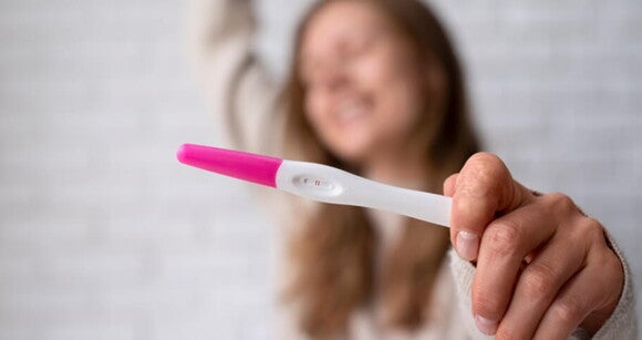 Mulher feliz segurando um teste de grávidez positivo Mulher feliz segurando um teste de grávidez positivo