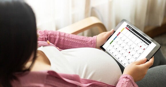 Mulher grávida sentada em uma cadeira segurando um calendário online Mulher grávida sentada em uma cadeira segurando um calendário online